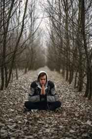 man wearing gray black zip hoodie jacket praying in between black tree during daytime